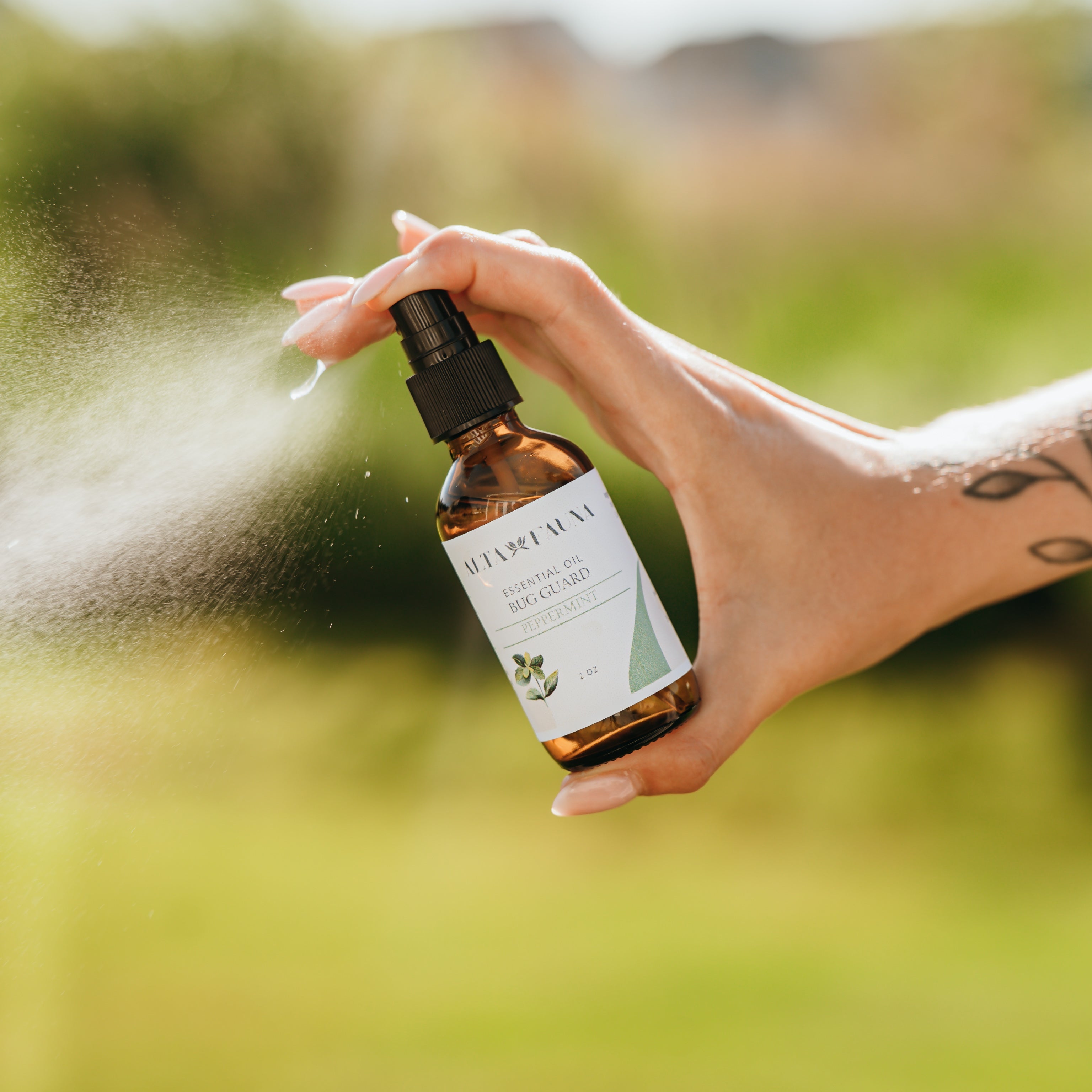 Alta Fauna Peppermint Bug Guard being held by a hand in an outdoor setting with a fine mist coming from the amber, glass spray bottle.