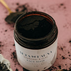 Alta Fauna charcoal and clay face mask in amber, glass jar with the lid off on a pink background.