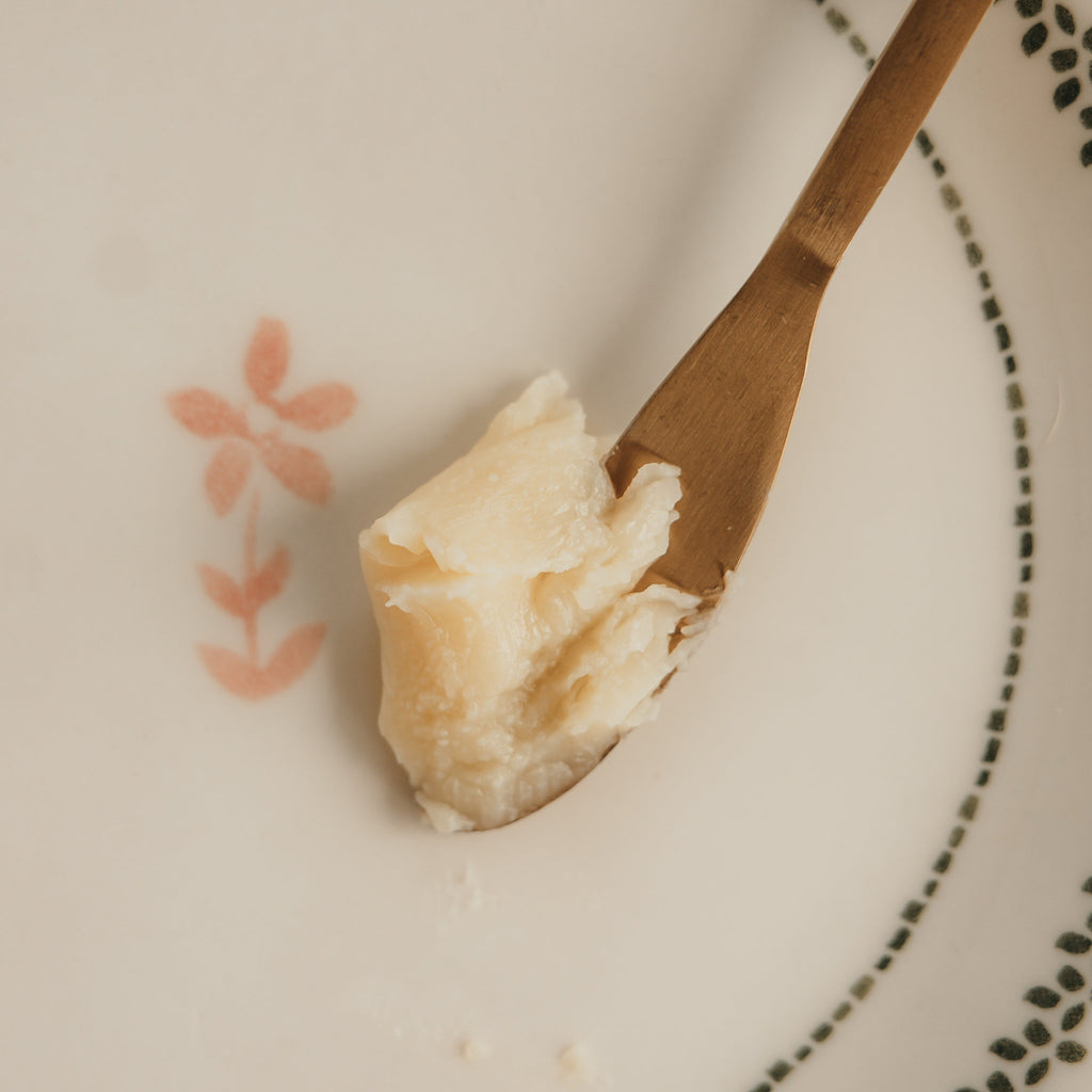 Wooden spoon with a scoop of Alta Fauna face cream on a white plate with floral designs