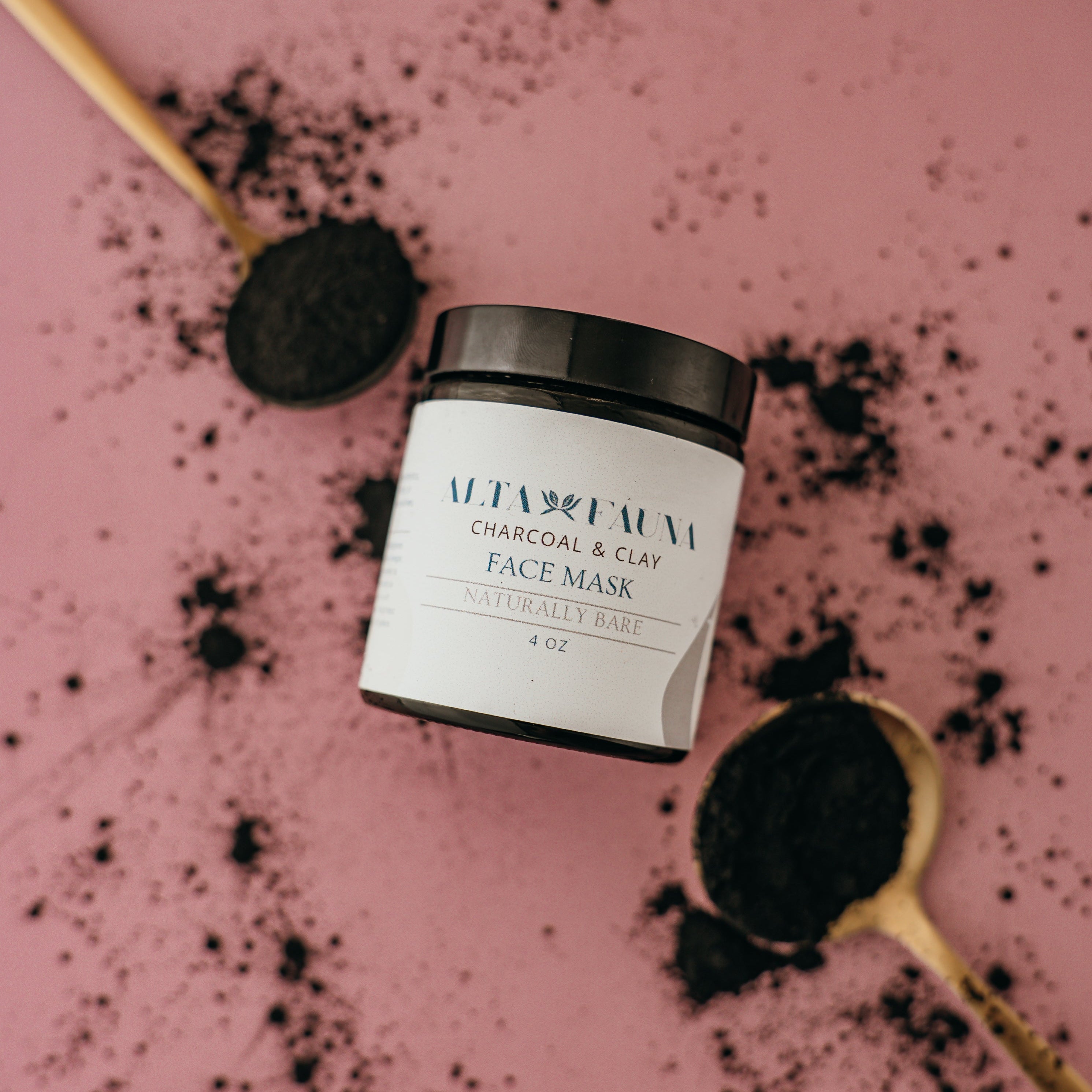 Jar of Charcoal and Clay Face Mask on a pink background with black powder.
