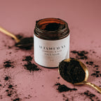 Alta Fauna charcoal and clay face mask jar next to a spoon with black powder on a pink background.