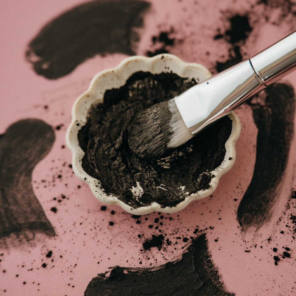 Alta Fauna charcoal and clay face mask in a small bowl with a brush on a pink background