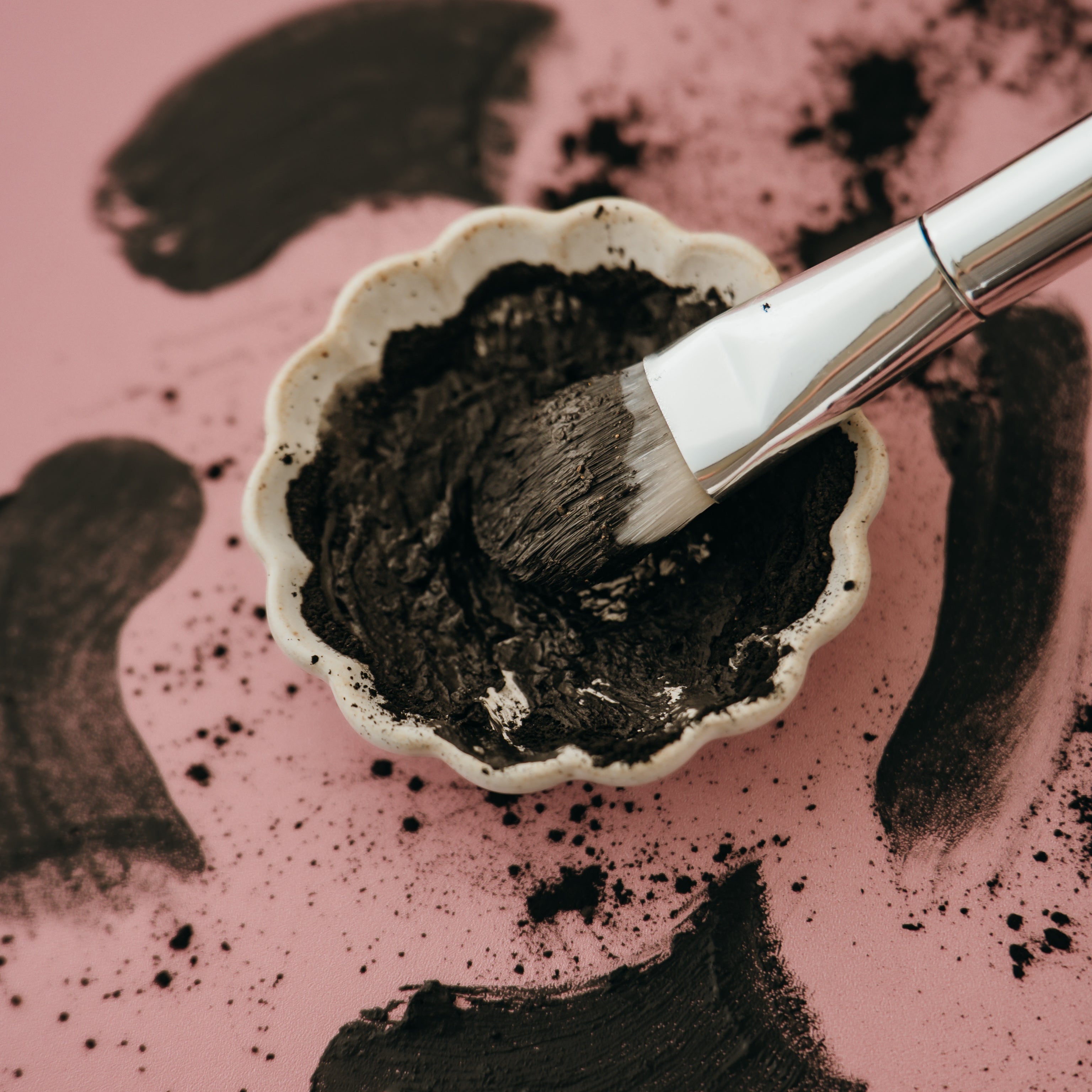 Alta Fauna charcoal and clay face mask in a small bowl with a brush on a pink background