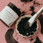 Alta Fauna Charcoal and clay face mask with a brush on a pink background.