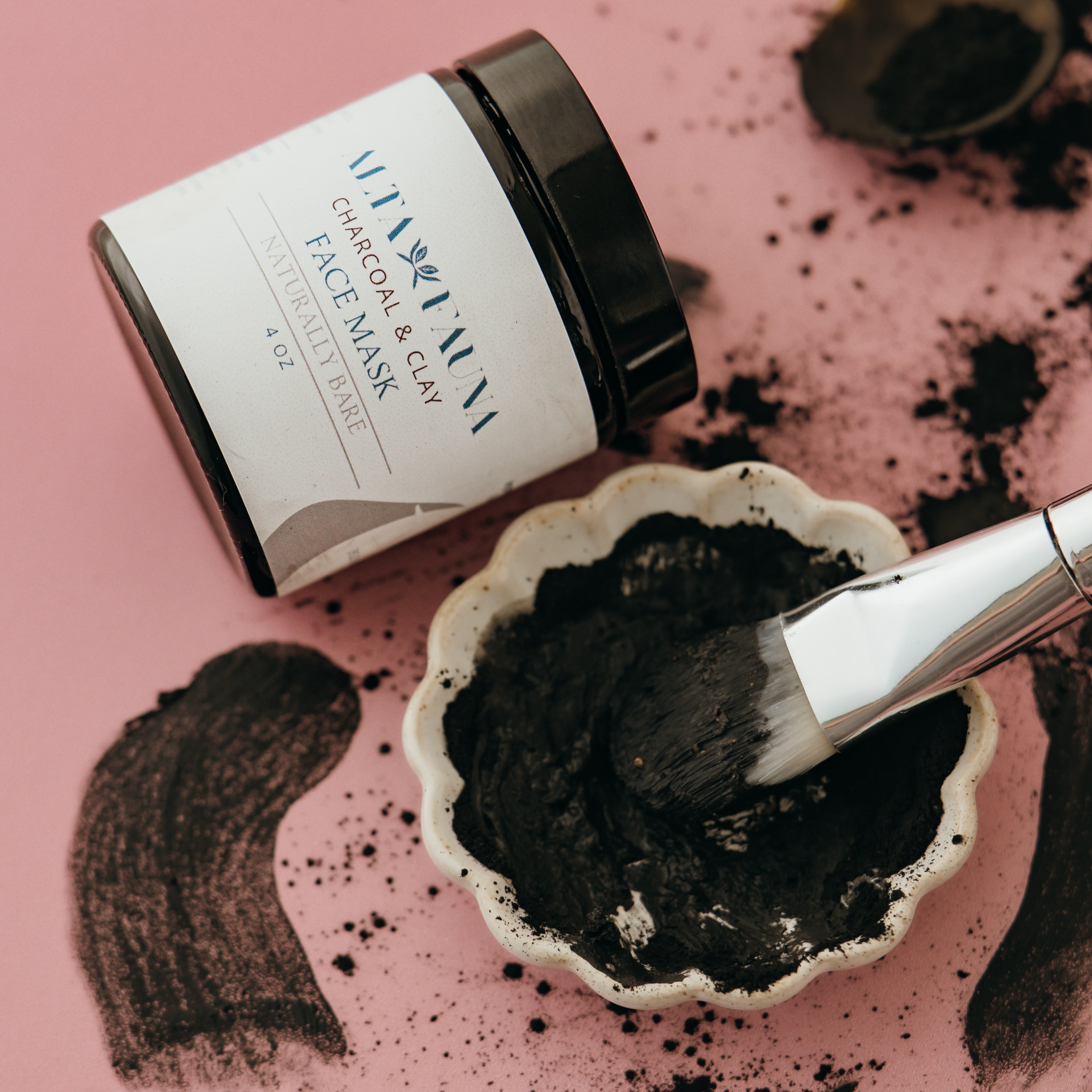 Alta Fauna Charcoal and clay face mask with a brush and wet product on a pink background