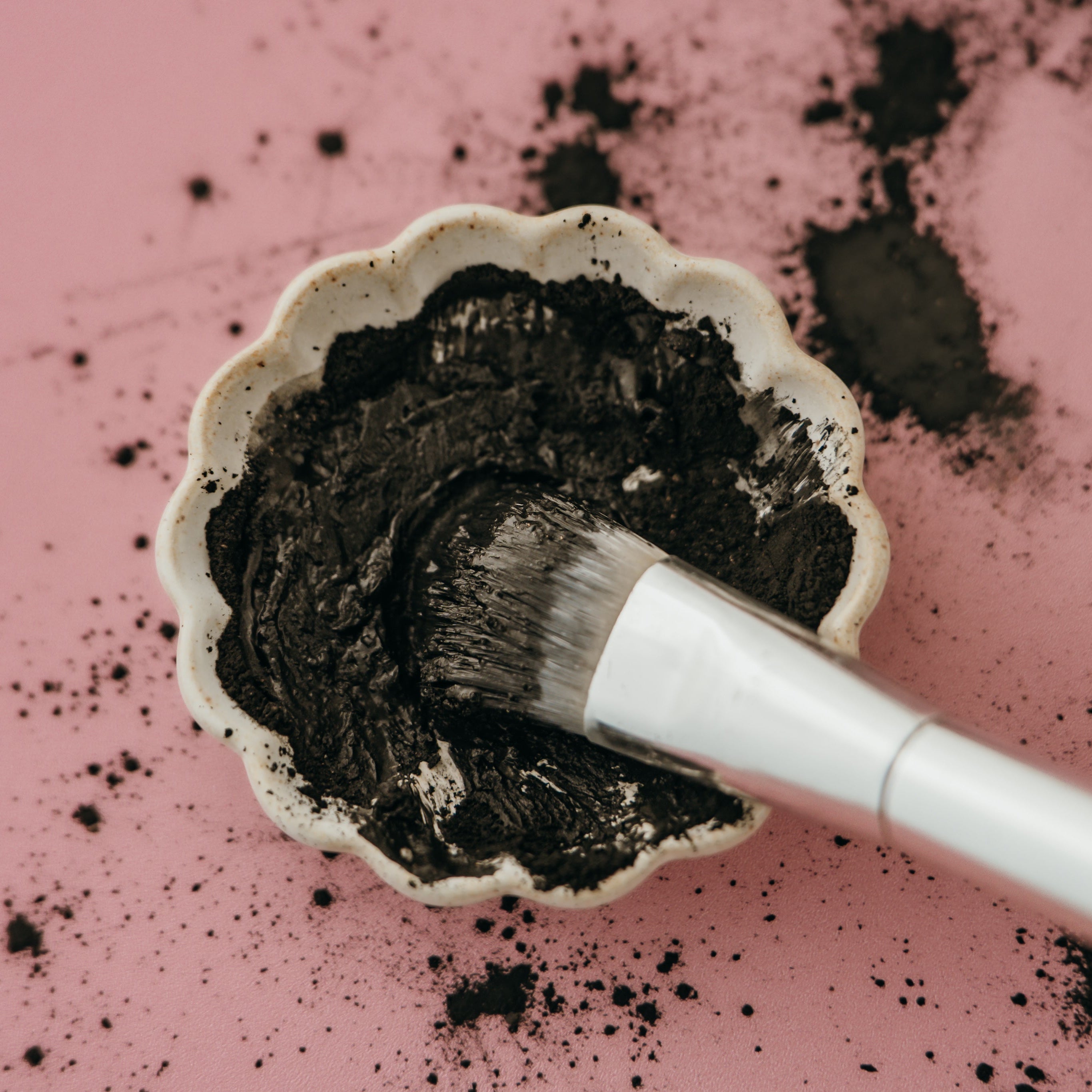 Alta Fauna charcoal and clay face mask with a brush on a pink background