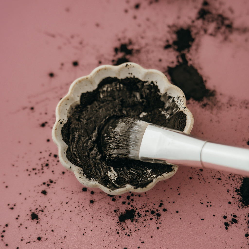 White bowl with dark powder and a brush on a pink background