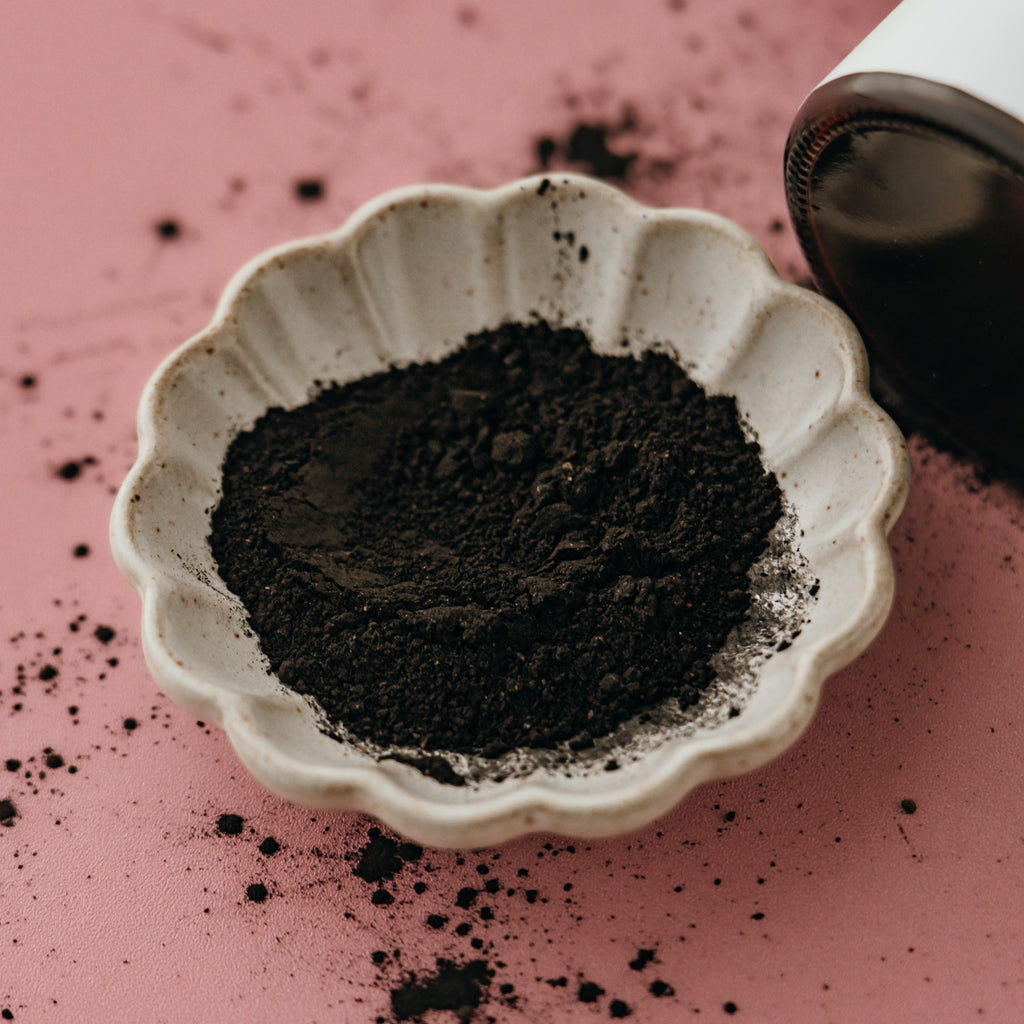 Small white dish filled with Alta Fauna charcoal and clay face mask on a pink surface