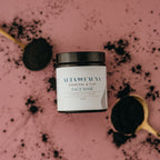 Alta Fauna charcoal and clay face mask jar next to a spoon with black powder on a pink background.
