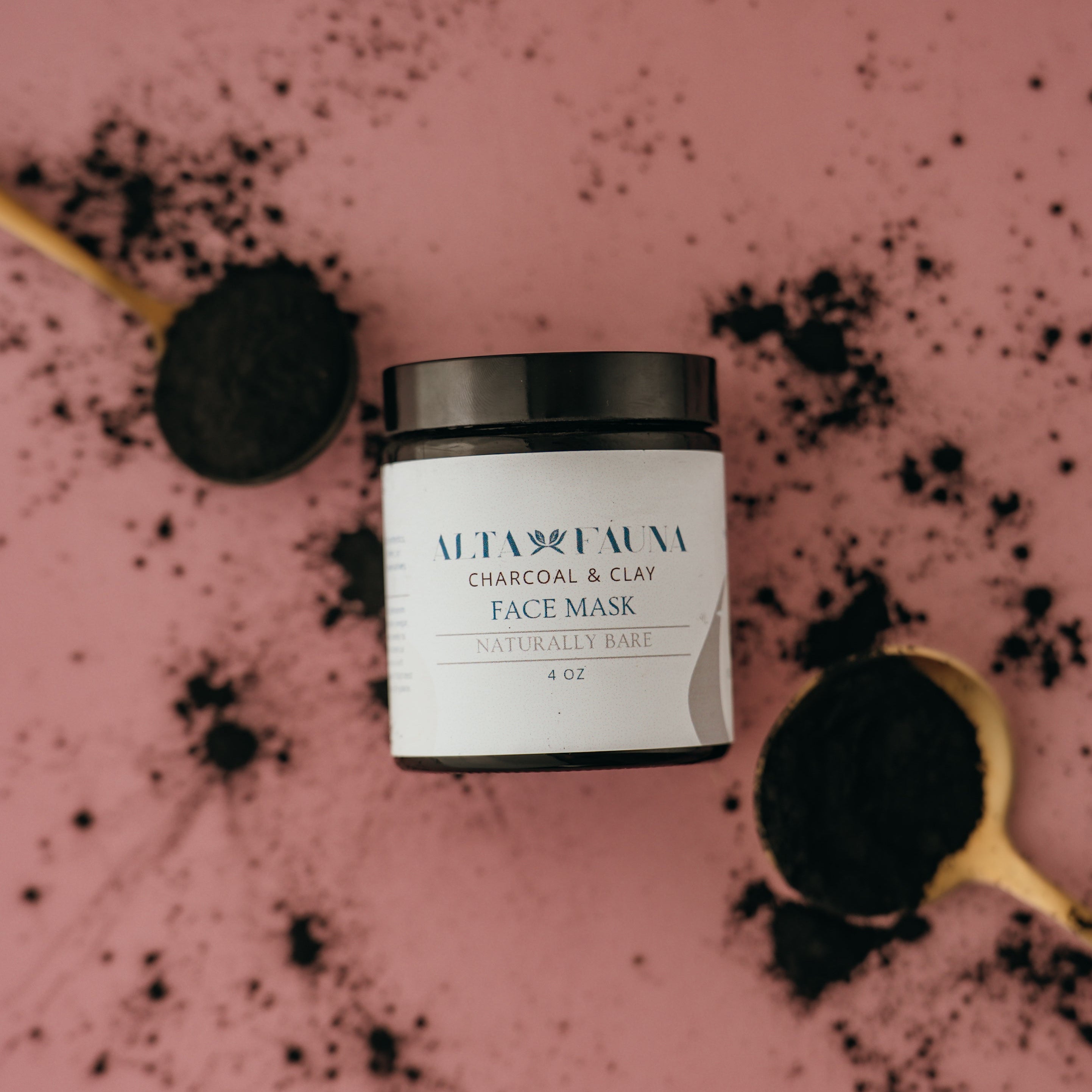 Alta Fauna charcoal and clay face mask jar next to a spoon with black powder on a pink background.