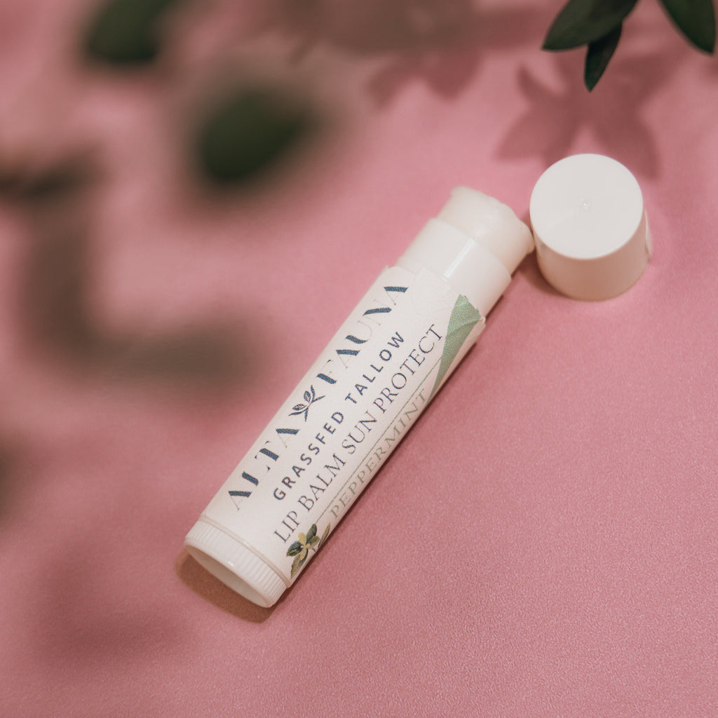 Close‑up of Alta Fauna Grassfed Tallow Lip Balm in Peppermint with mineral zinc for protective daily lip care. Close up of tube and lip balm texture on pink background.