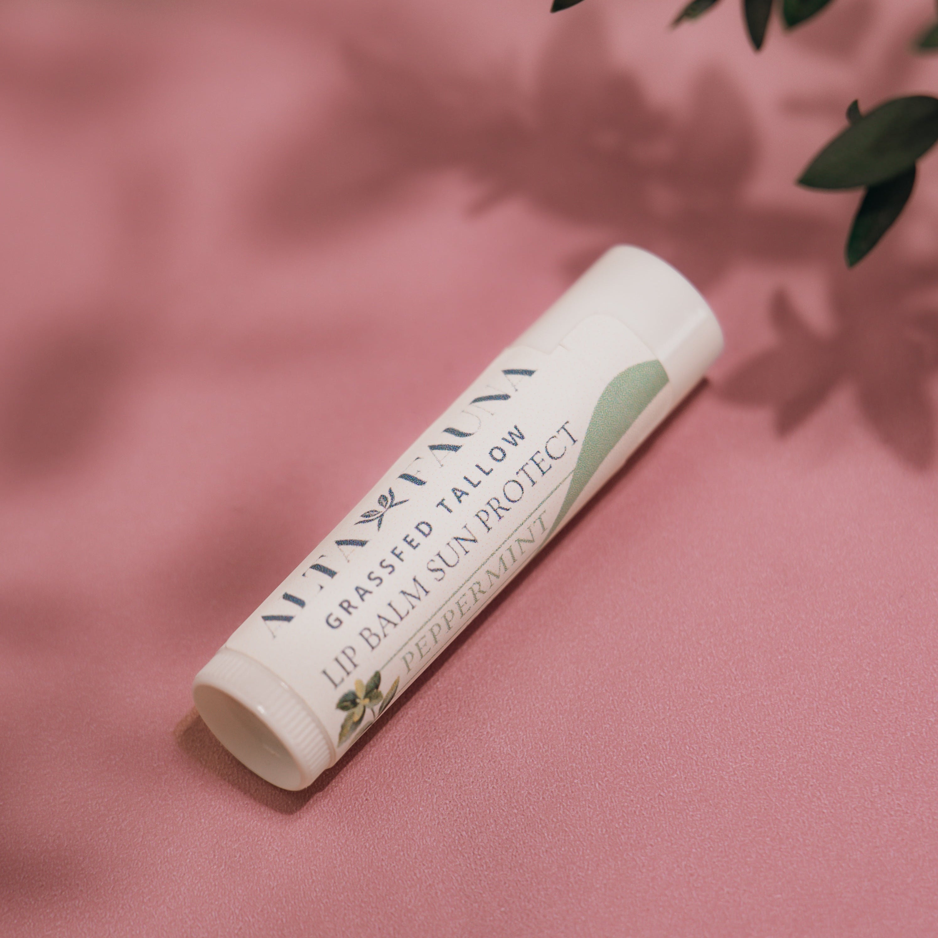 Alta Fauna Peppermint Lip Balm with Sun Protect with lid on a pink background.  Texture of lip balm shown. 