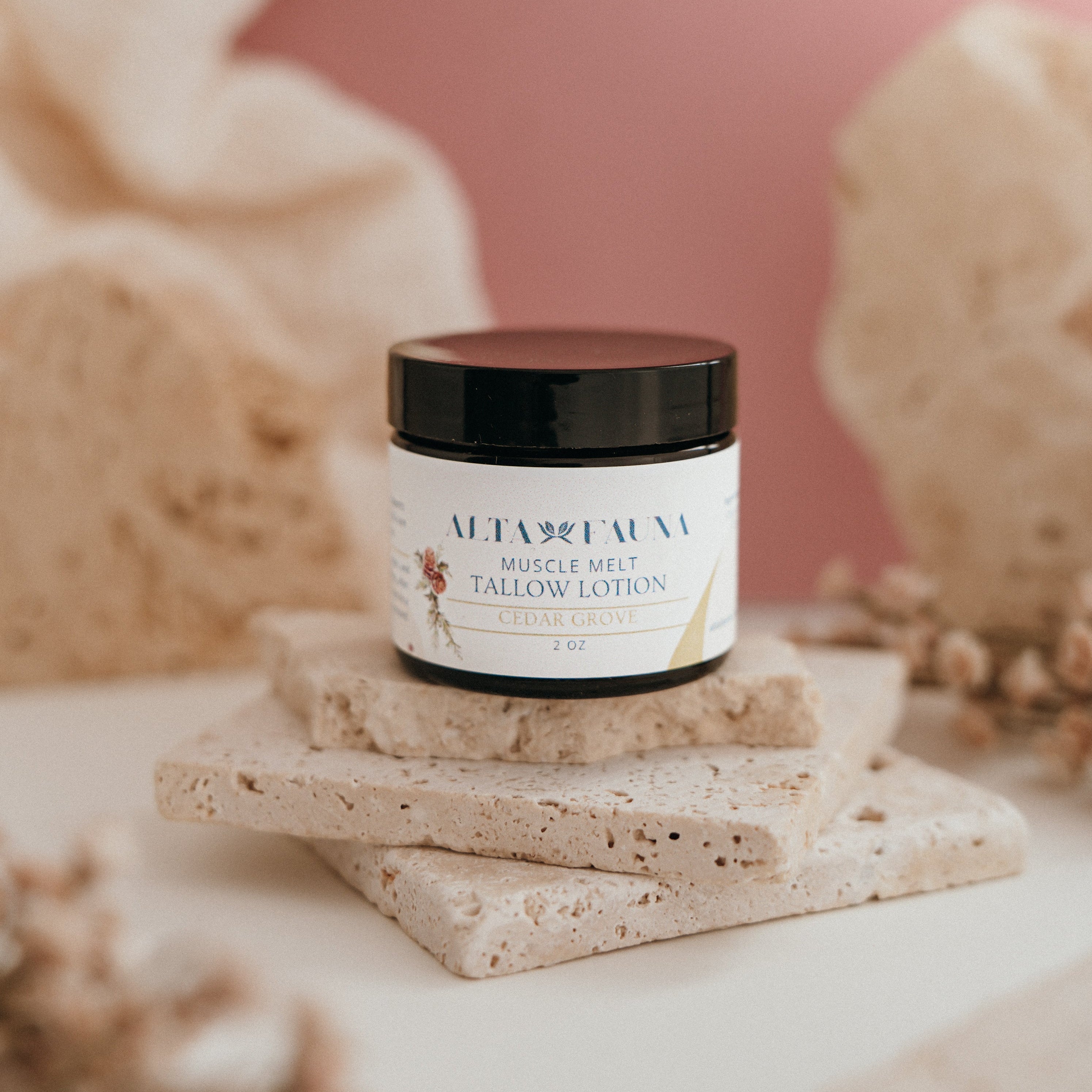 Alta Fauna Muscle Melt Tallow Lotion in Cedar Grove (2oz) pictured on a stack of granite with a light pink background.
