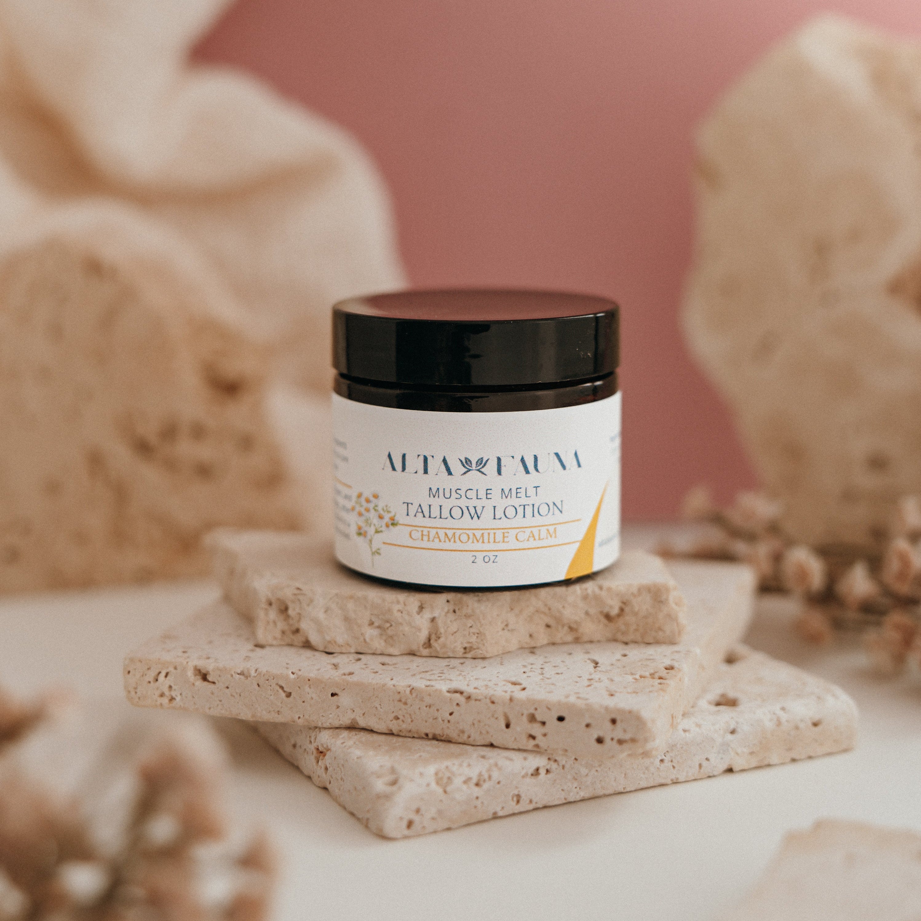 Alta Fauna Muscle Melt Tallow Lotion in Chamomile Calm (2oz) pictured on a stack of granite with a light pink background.