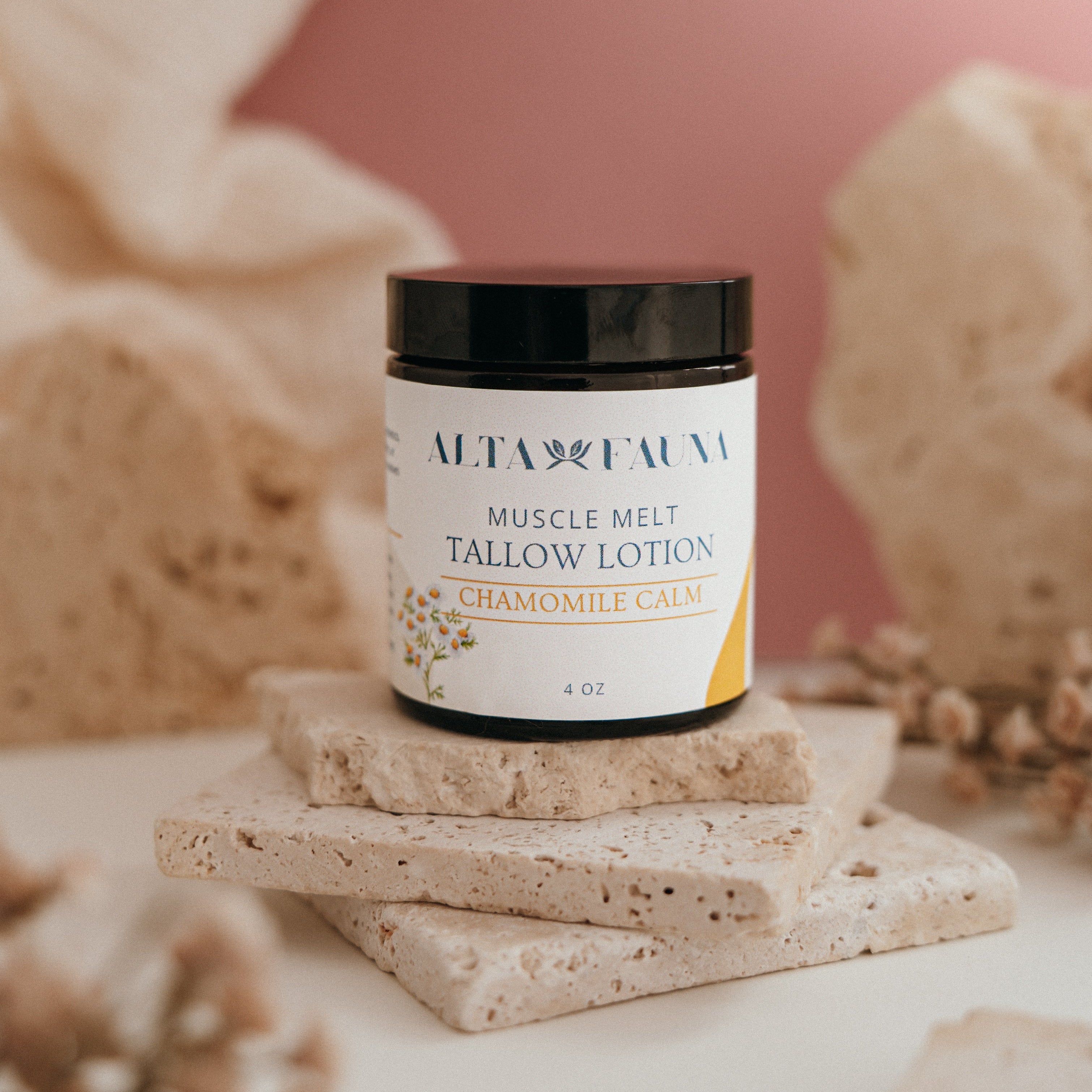 Alta Fauna Muscle Melt Tallow Lotion in Chamomile Calm (4oz) pictured on a stack of granite with a light pink background.