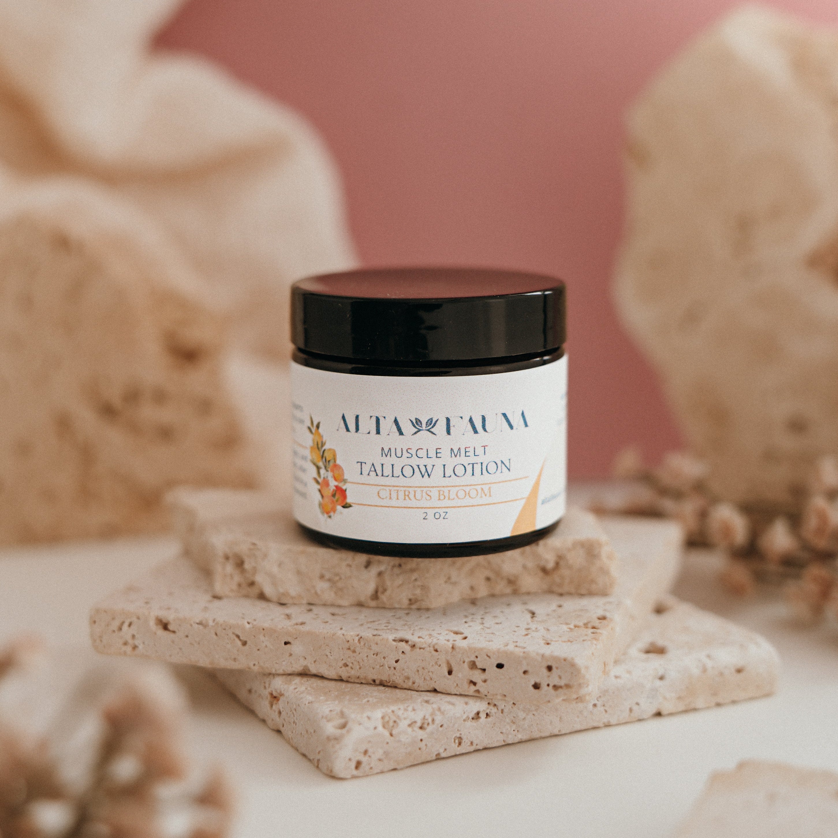 Alta Fauna Muscle Melt Tallow Lotion in Citrus Bloom (2oz) pictured on a stack of granite with a light pink background.