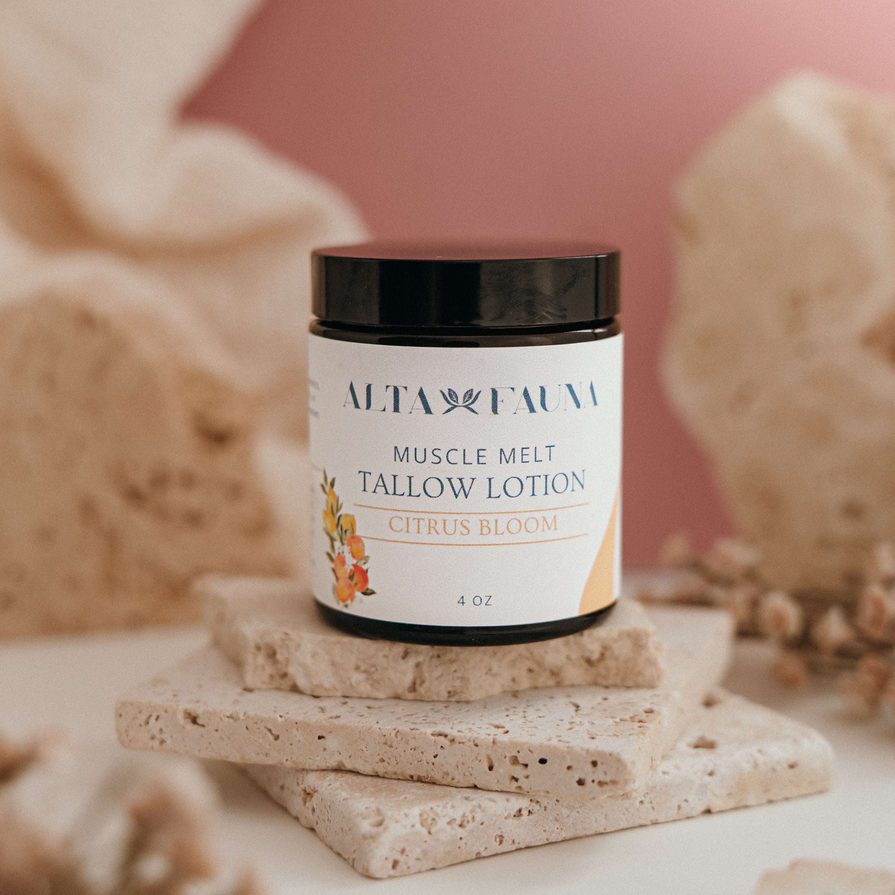 Alta Fauna Muscle Melt Tallow Lotion in Citrus Bloom (4oz) pictured on a stack of granite with a light pink background.