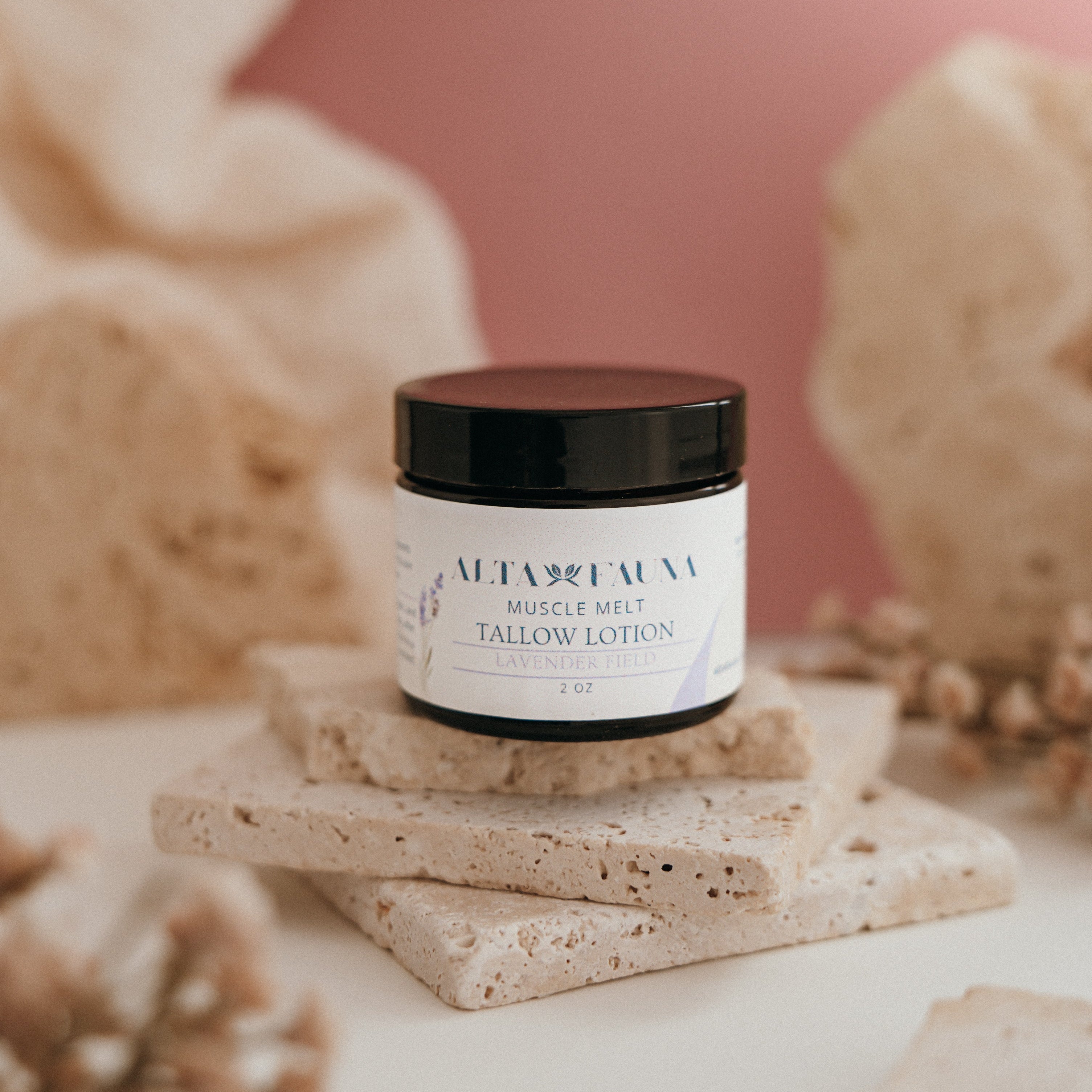 Alta Fauna Muscle Melt Tallow Lotion in Lavender Field (2oz) pictured on a stack of granite with a light pink background.
