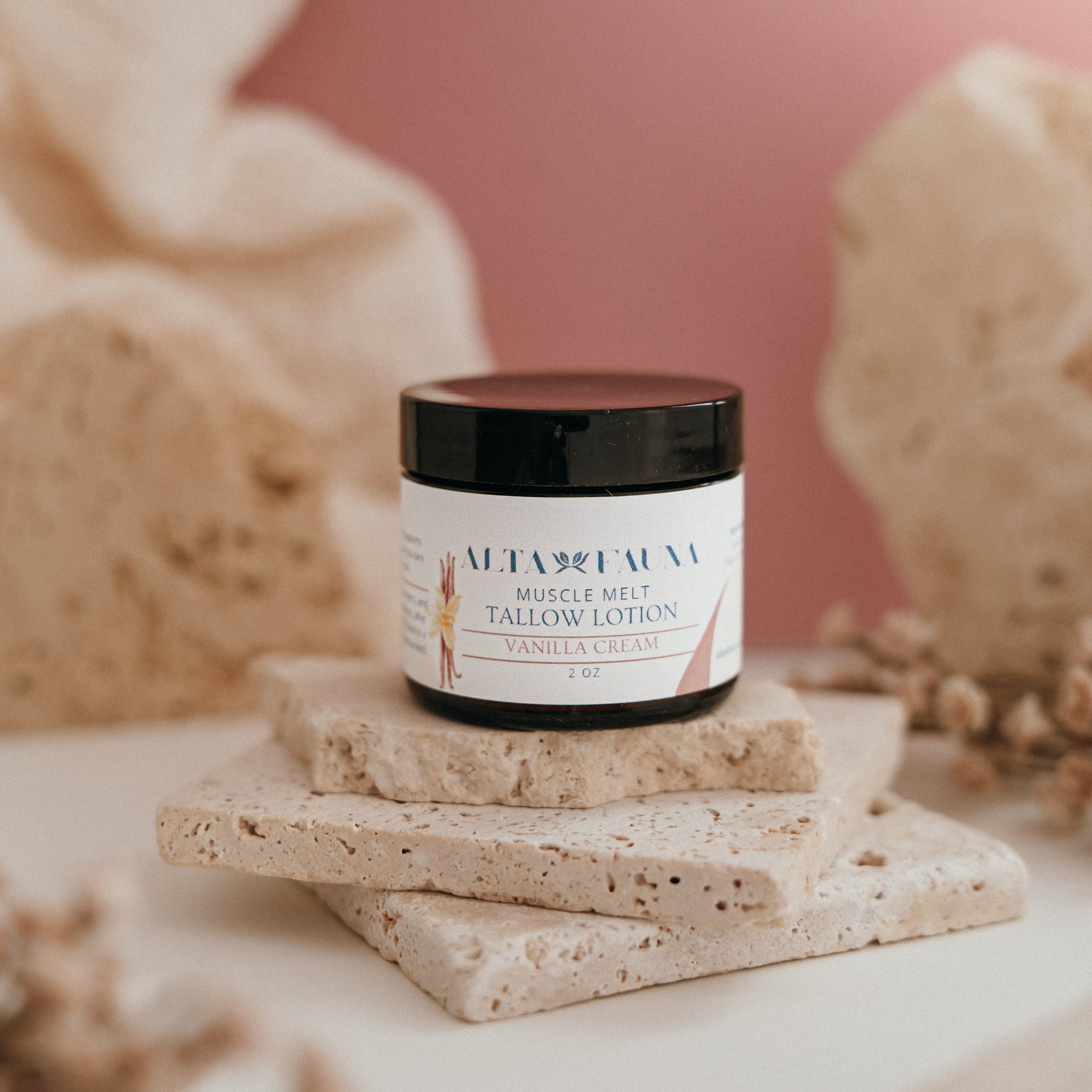 Alta Fauna Muscle Melt Tallow Lotion in Vanilla Cream (2oz) pictured on a stack of granite with a light pink background.