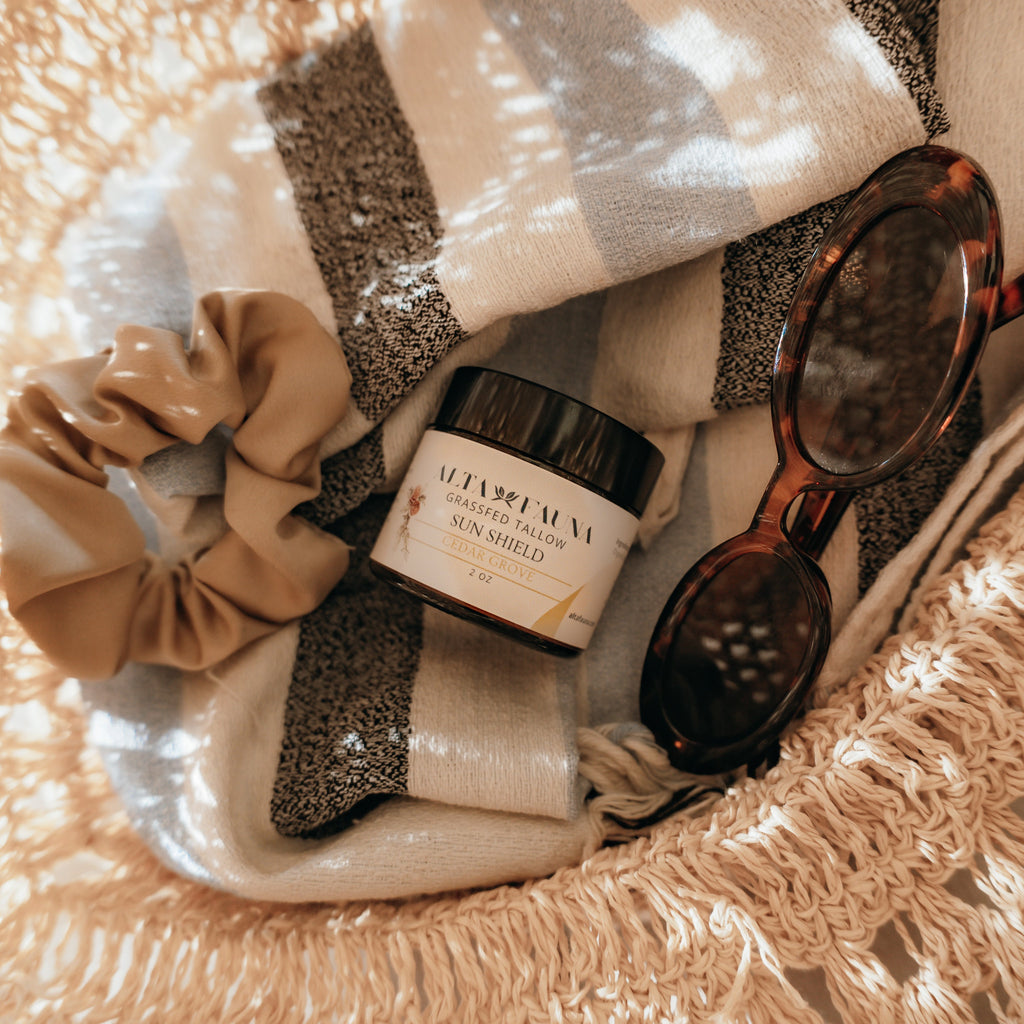 Basket with Alta Fauna Sun Shield lotion, scrunchie, and sunglasses on a beach towel.