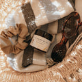 Basket with Alta Fauna Sun Shield lotion, scrunchie, and sunglasses on a beach towel.
