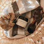 Basket with Alta Fauna Sun Shield lotion, scrunchie, and sunglasses on a beach towel.