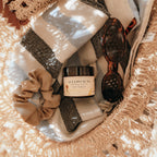 Basket with Alta Fauna Sun Shield lotion, scrunchie, and sunglasses on a beach towel.