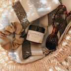 Basket with Alta Fauna Sun Shield lotion, scrunchie, and sunglasses on a beach towel.