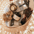 Basket with Alta Fauna Sun Shield lotion, scrunchie, and sunglasses on a beach towel.