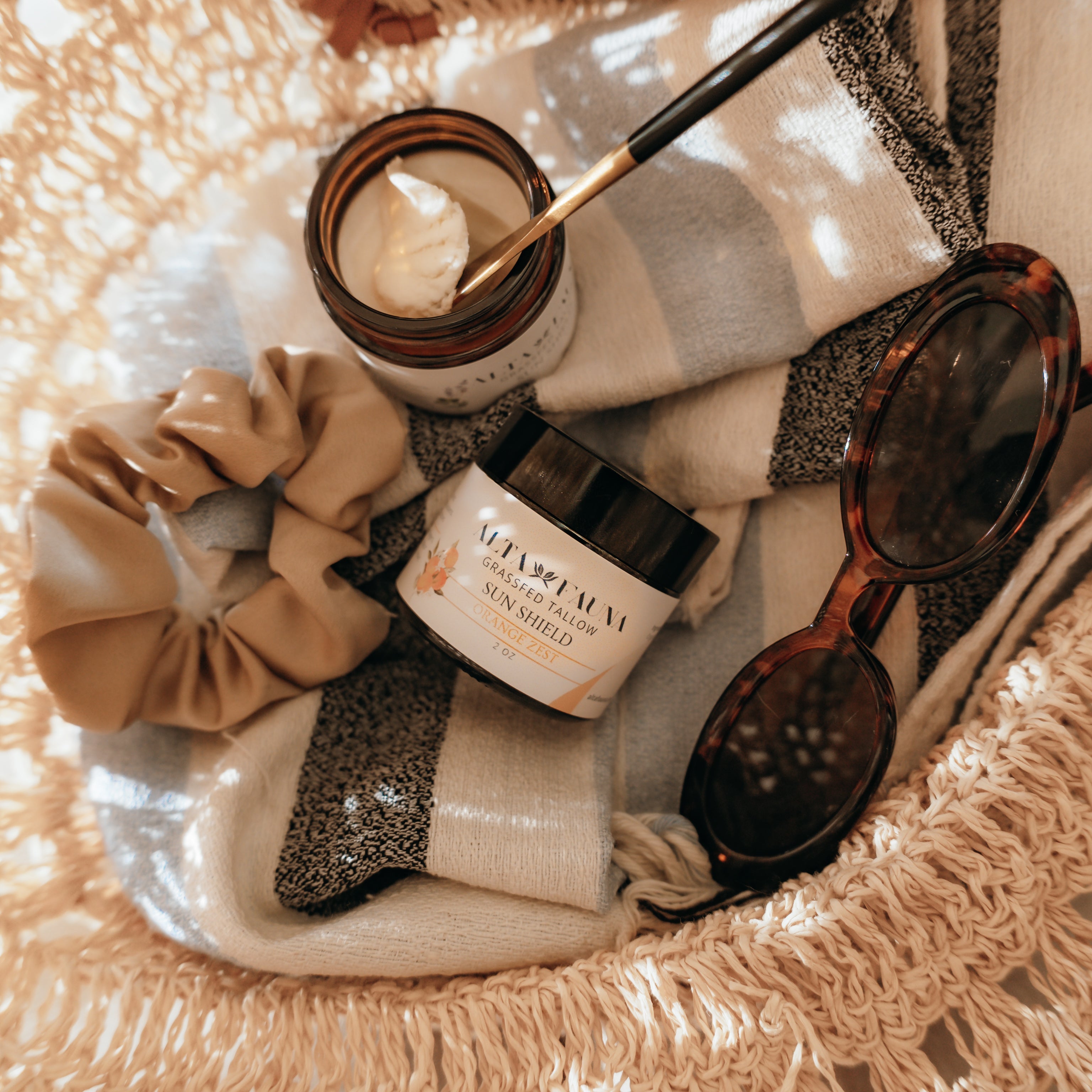 Basket with Alta Fauna Sun Shield lotion, scrunchie, and sunglasses on a beach towel.