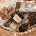 Basket with Alta Fauna Sun Shield lotion, scrunchie, and sunglasses on a beach towel.